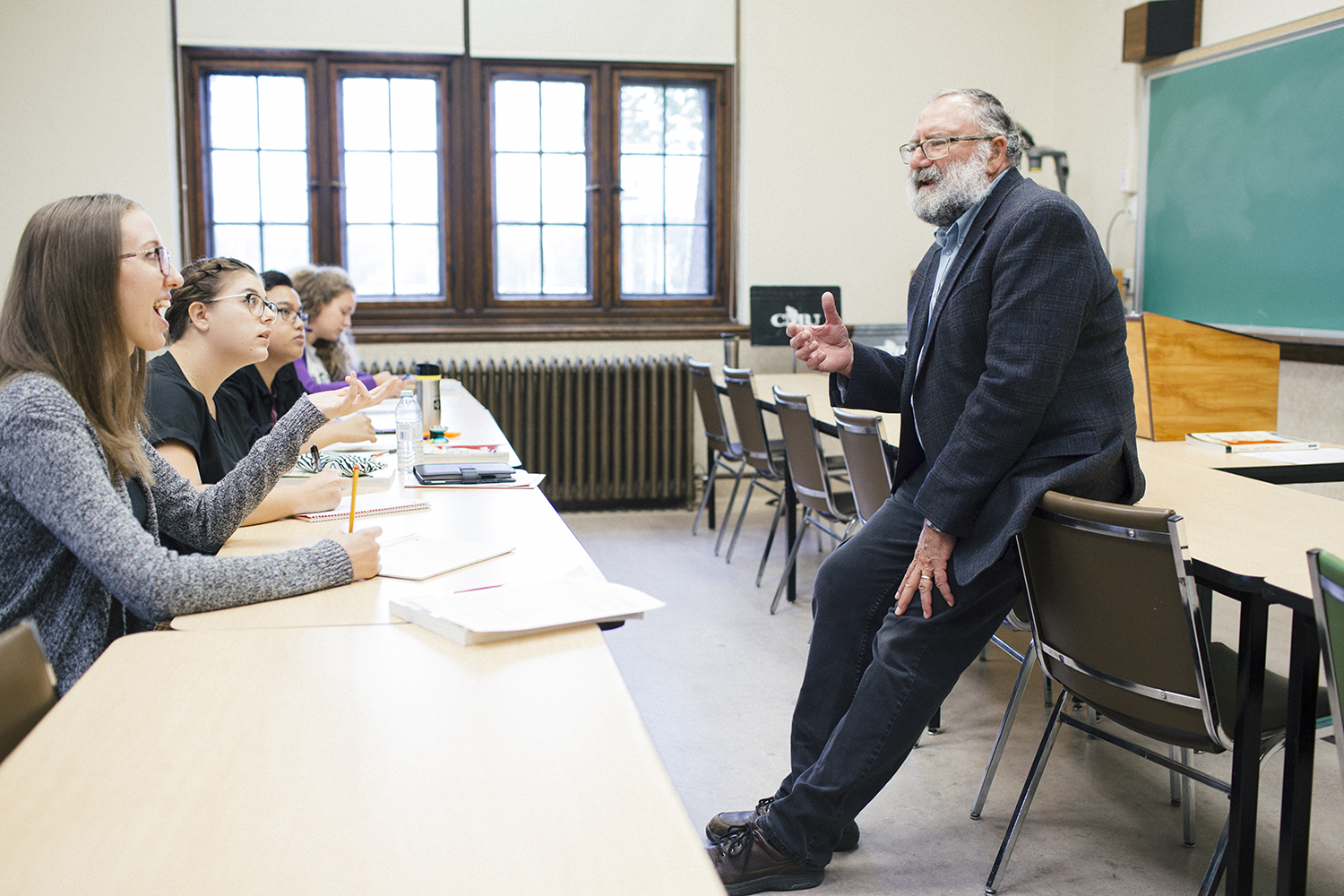 Students seated at a desk in small classroom at CMU, engaging with a professor across from them.