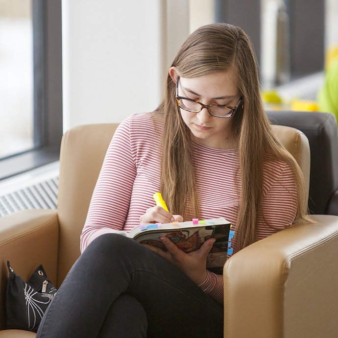 6 study tips — A student sits by the window in the CMU Library highligher in hand, reading a text book.