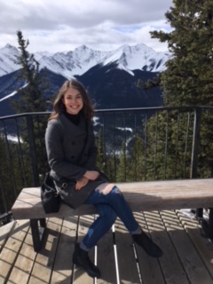 Anika Loeppky sits on a bench with white rocky mountain peaks in the background.